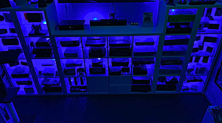 ikea kallax hack to use glass pane for video game console storage cabinet. cabinet back lit in blue with more than two dozen video game consoles